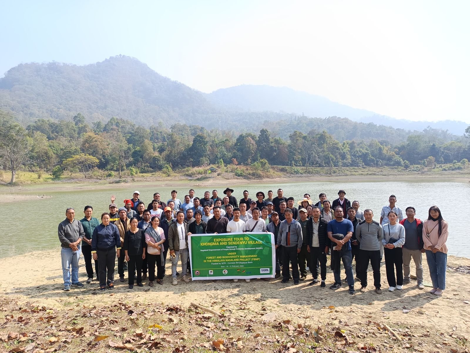A large group behind a banner for an exposure tour to Khonoma and Sendenyu villages