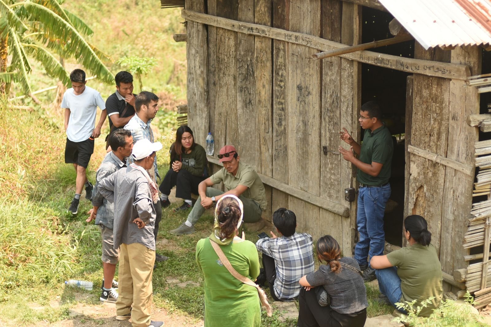 A trainer briefing a group beside a wooden hut in the forest