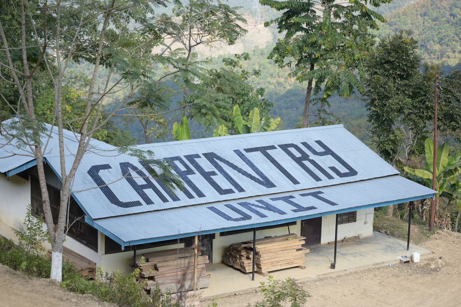 The carpentry unit from above, its roof lettered CARPENTRY UNIT, timber stacked under the eaves