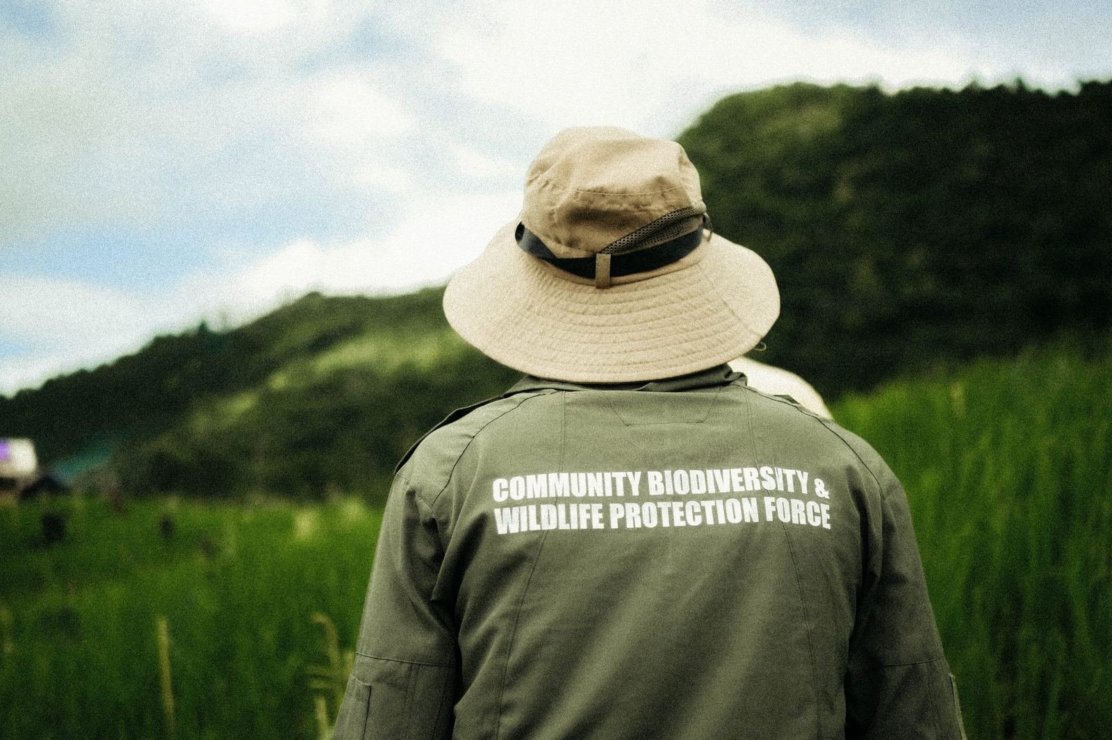 A community monitor in a Community Biodiversity and Wildlife Protection Force jacket looking over the hills