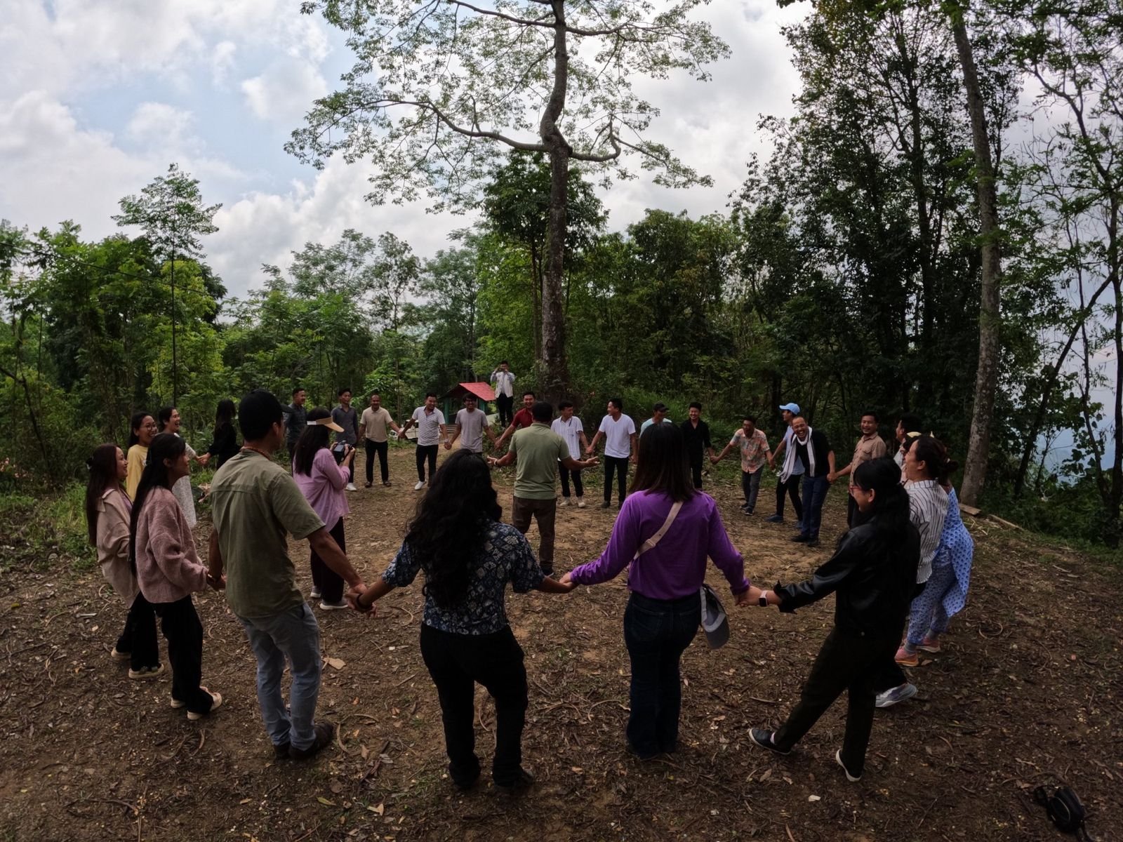 Participants holding hands in a wide circle under the trees