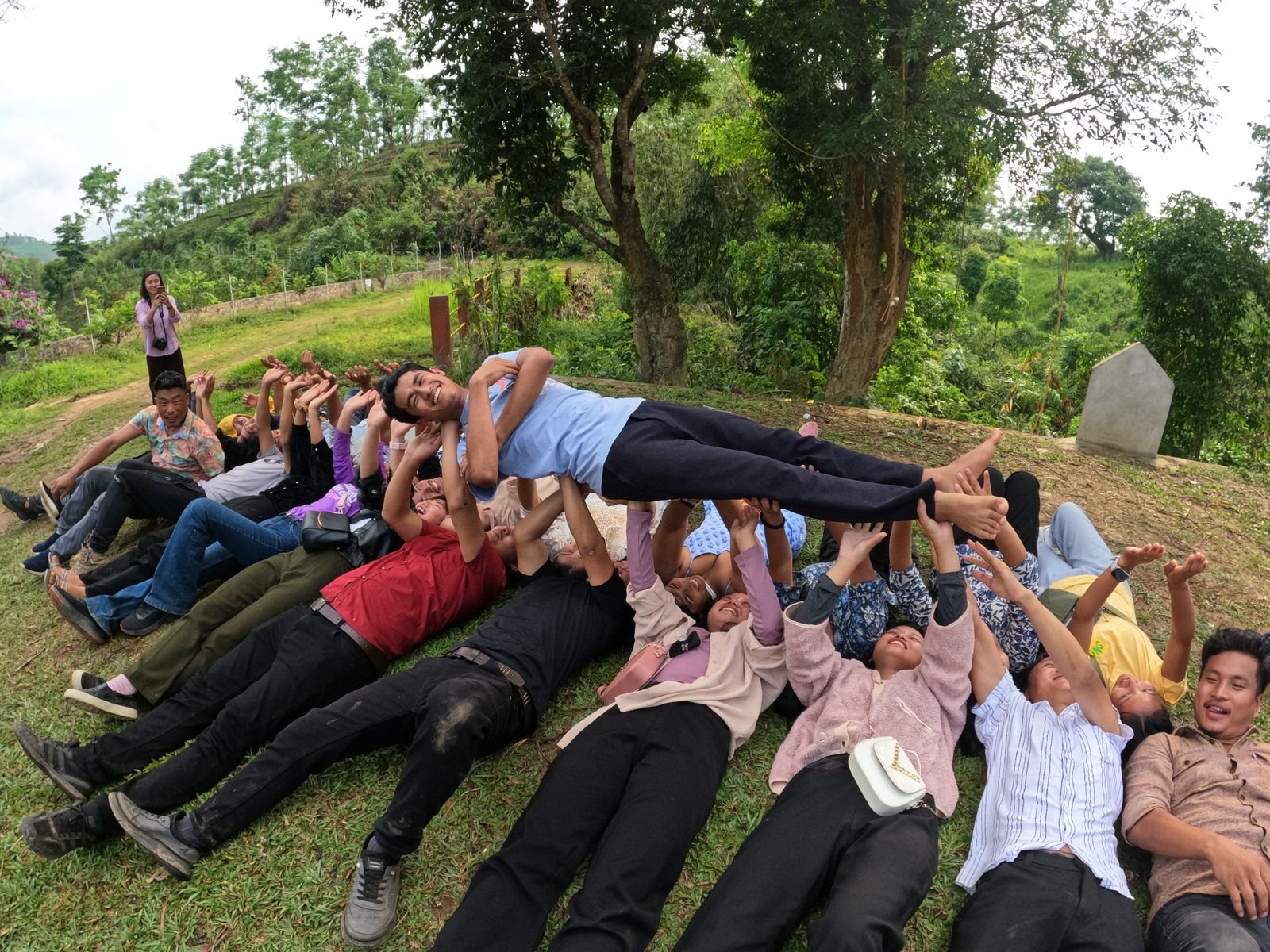 A group lying on the grass lifting one person on their raised hands